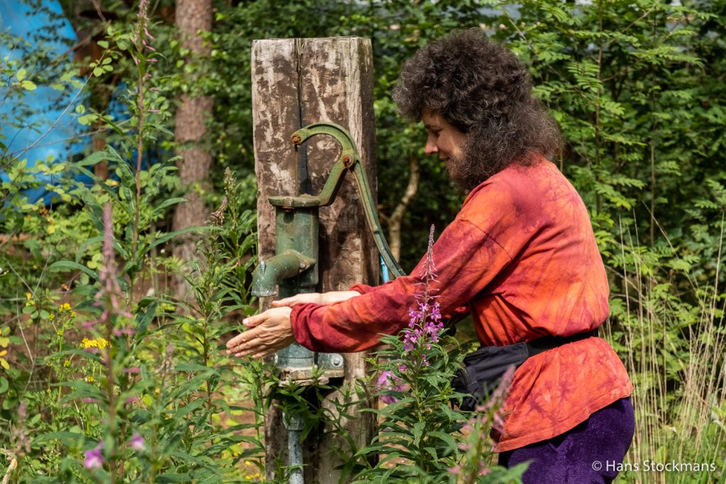 Marieke in haar bloementuin, aan de oude pomp.